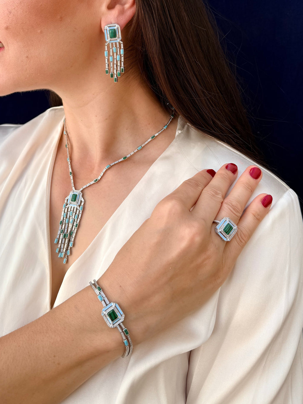 Woman wearing a set of silver jewelry with green gemstones against a dark background