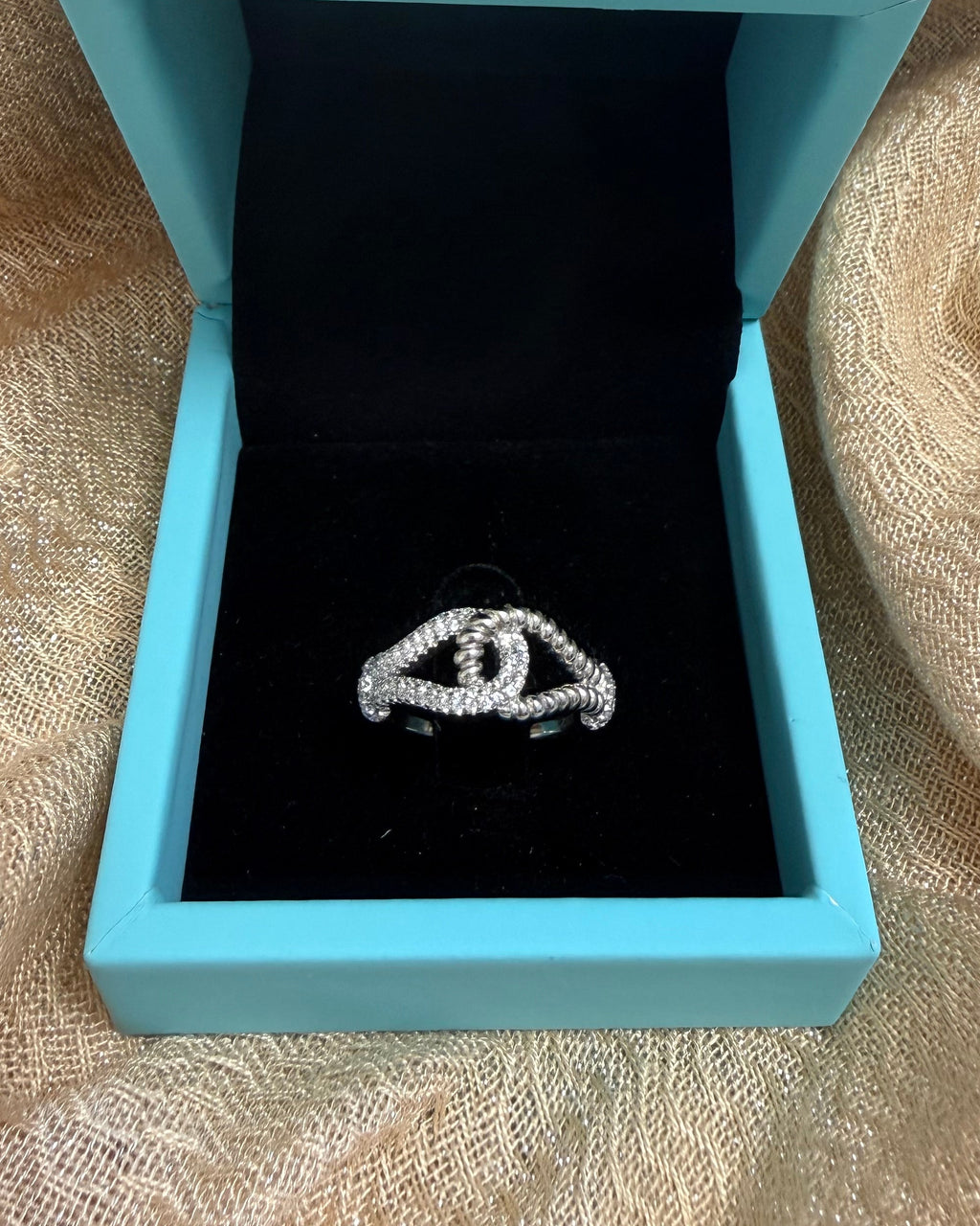 Blue jewelry box with a black interior containing a silver ring on a beige fabric background