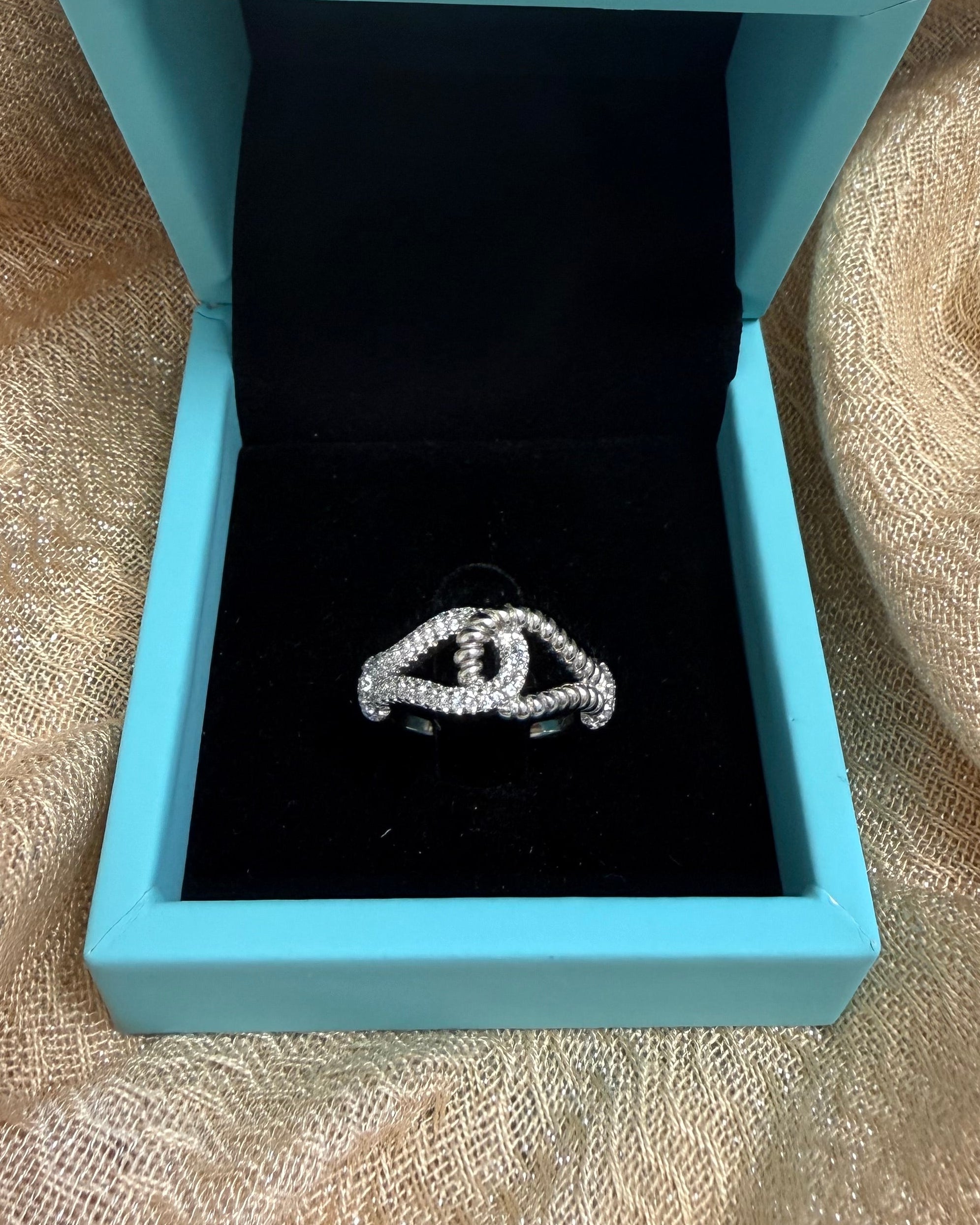 Blue jewelry box with a black interior containing a silver ring on a beige fabric background