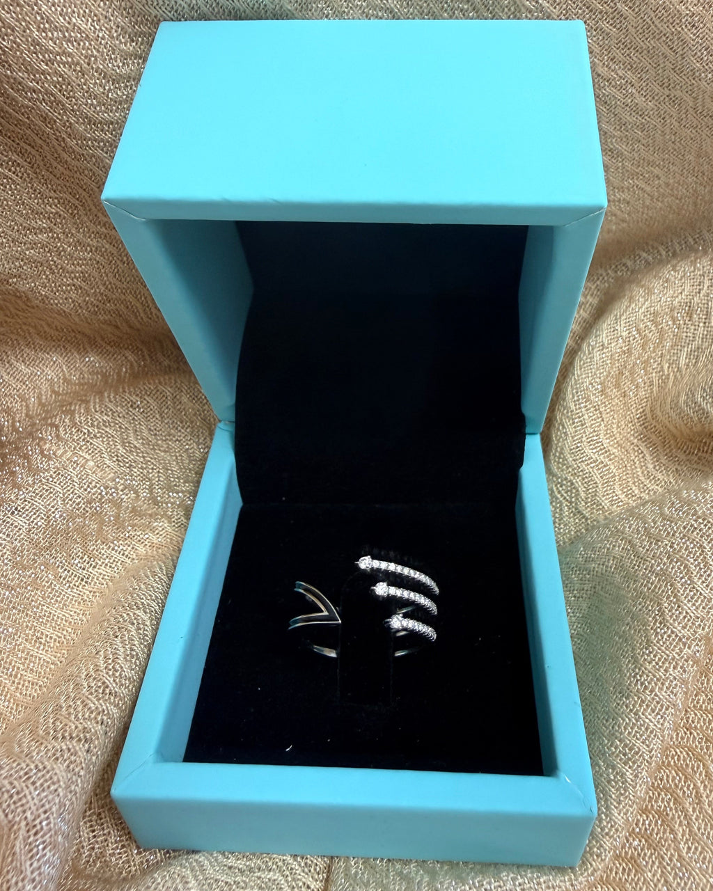 Light blue jewelry box with a black interior on a textured beige surface